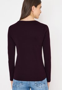 Langærmet top i dyb lilla stof, glat tekstur, med en rund halsudskæring og en tætsiddende pasform, parret med lyseblå denim jeans.