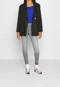 Blazer negro de doble botonadura, top azul, jeans skinny gris claro, zapatillas blancas y naranjas con detalles en negro. Atuendo casual con colores contrastantes.