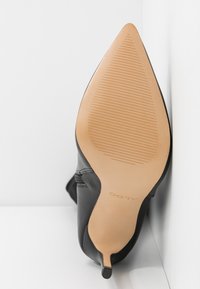 Semelle d'une botte noire à bout pointu avec un petit talon, semelle en caoutchouc beige texturée, et le logo "ALDO" visible près du talon.