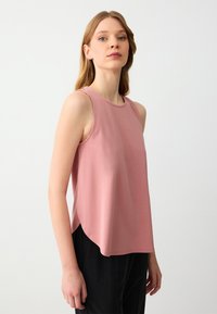 Top senza maniche rosa con scollatura rotonda e vestibilità rilassata. Il tessuto sembra morbido con una leggera lucentezza, presenta spacchi laterali per facilitare i movimenti.
