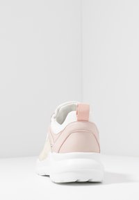 Sneaker avec un empeigne en cuir rose et un panneau en textile crème, semelle extérieure en caoutchouc blanc et un tirant rose à l'arrière, présentant une forme arrondie.