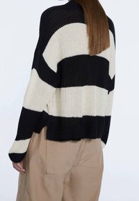 Maglione a righe in maglia con colori nero e crema, vestibilità larga, polsini e orlo a coste. La texture è spessa e traspirante.