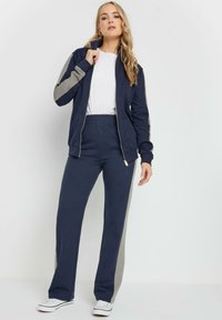 Set di tuta blu navy con dettagli grigi, composto da una giacca con zip e pantaloni con vita elastica, realizzato in tessuto liscio ed elasticizzato.