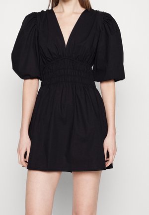 Woman wearing a black short dress with puffed elbow-length sleeves, deep V-neckline, and cinched waistband.