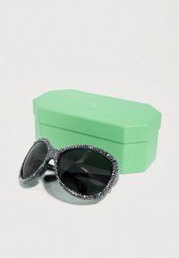 Μαύρα γυαλιά ηλίου με πλαίσιο διακοσμημένο με υφή και στρας, συνοδευόμενα από μια οκταγωνική θήκη σε μέντα πράσινο χρώμα. Οι φακοί είναι σκουροί.