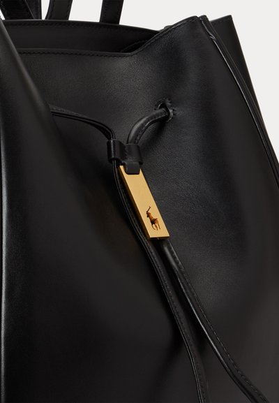 Μαύρη δερμάτινη τσάντα χειρός με κλείσιμο κορδονιού και ένα χρυσό ορθογώνιο γούρι με ανάγλυφη σιλουέτα παίκτη πόλο.