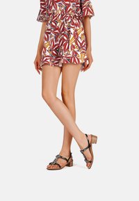 Sandali in pelle nera con tacco a blocco, adornati con decorazioni ornamentali, abbinati a una tuta a fantasia colorata.