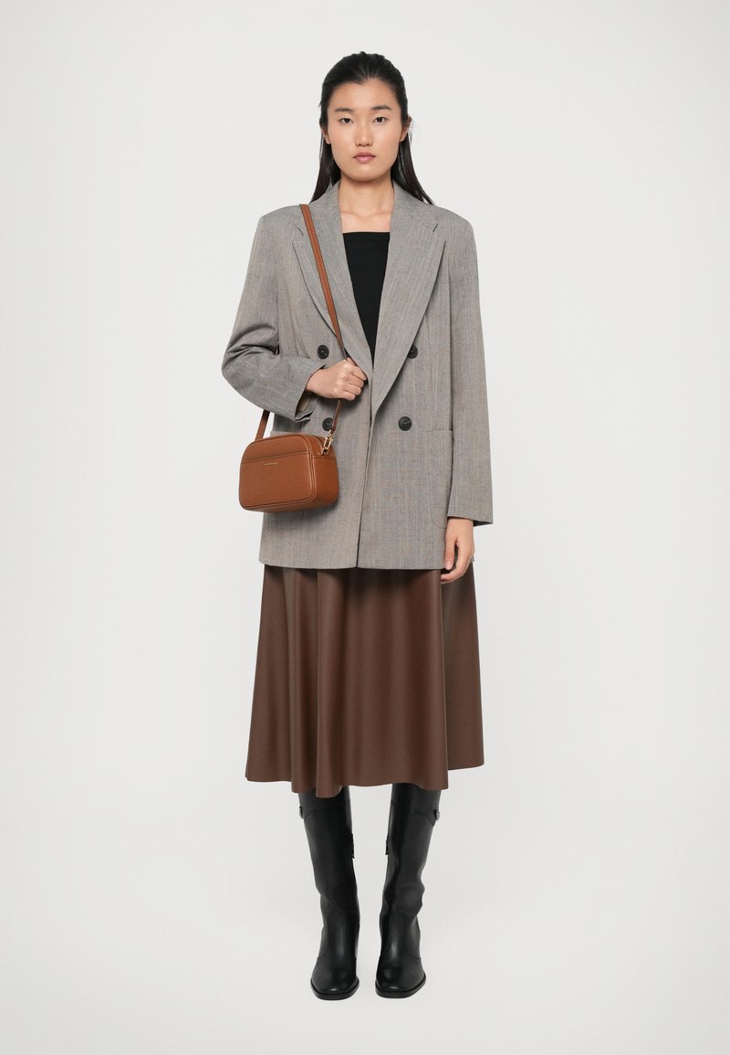 Blazer grigio doppiopetto, gonna di raso marrone e stivali alti in pelle nera. Borsa a tracolla marrone con chiusura zip e forma rettangolare.