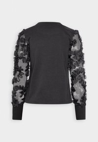 Top negro de manga larga con cuerpo liso y mangas abullonadas transparentes adornadas con volantes superpuestos. Los puños acanalados completan el diseño.