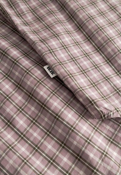 Tela de algodón de color púrpura claro con un patrón de cuadros en blanco y verde oscuro, con una pequeña etiqueta cosida en el borde.