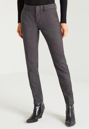 Femme portant un pantalon gris texturé coupe slim, associé à des bottines compensées noires à bout pointu et un haut à manches longues côtelé noir.
