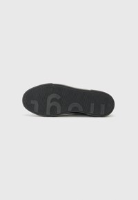 Suola di scarpa in gomma nera con una superficie texturizzata, dotata di un logo pronunciato e di un motivo a coste per una migliore aderenza. Forma piatta e allungata.