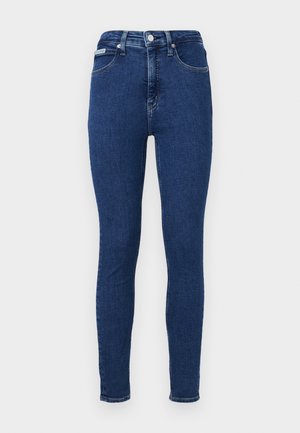Jeans ajustados de mezclilla azul oscura. Diseño de cintura alta con cinco bolsillos, trabillas para el cinturón y costuras en contraste. Textura suave con ligero estiramiento.