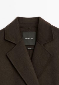 Tmavohnědý vlněný kabát s klopovým límcem. Obsahuje štítek s nápisem "Massimo Dutti." Měkká textura, žádné viditelné zapínání nebo vzory.
