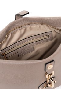 Interior de un bolso de cuero gris con cremallera dorada y bolsillo; textura suave y diseño minimalista. Presenta un forro de tela beige y una etiqueta de marca.