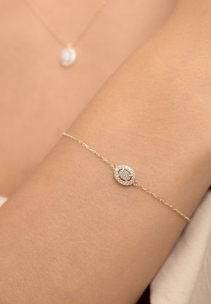 Gold chain bracelet featuring a central oval charm, adorned with a circle of small crystals and a rose gold accent in the center.