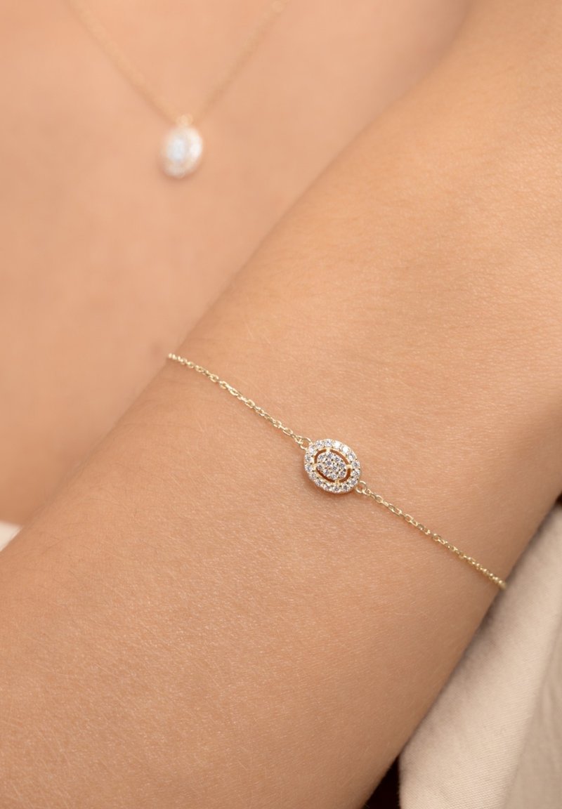 Gold chain bracelet featuring a central oval charm, adorned with a circle of small crystals and a rose gold accent in the center.