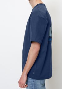 Camiseta de algodón azul marino con un corte amplio, mangas cortas y escote redondo. Presenta una impresión gráfica en la parte posterior.