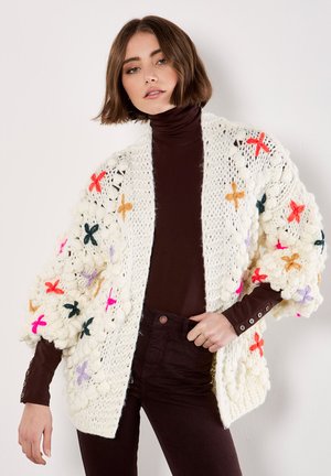 Füllige weiße Strickjacke mit bunten gestickten Blumen in Rot, Orange, Pink und Grün. Hat lockere, strukturierte Ärmel.
