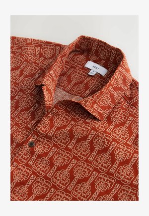 Īsroku krekls rūsganā krāsā ar baltu ģeometrisku rakstu; tam ir apkaklīte un melns pogas aizdare pie apkakles malas.