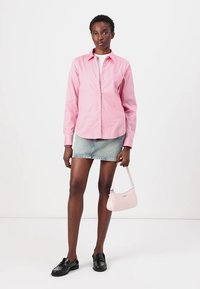 Camicia button-up rosa pallido, gonna mini in denim, mocassini neri e una piccola borsa rosa. Tessuto morbido, vestibilità su misura e accenti sottili.