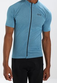 Cyklistický dres s krátkým rukávem z texturované modré látky s předním zipem a logem GORE, doplněný černými polstrovanými cyklistickými šortkami.