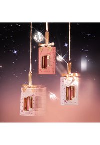 Tre set di lucidalabbra in scatola appesi, con confezioni rosa e bianche decorate con accenti dorati e fiocchi, featuring decorazioni a forma di disco riflettente.