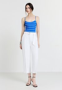 Body blu e bianco a righe abbinato a pantaloni bianchi a vita alta con cintura, completato da sandali neri con tacco.