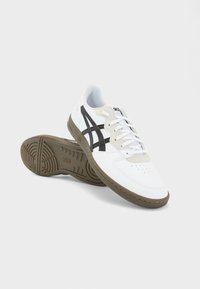Pantofi sport albi cu dungi negre, partea superioară din piele texturată, design cu șireturi și talpă din cauciuc cu un sistem de profil.