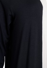 Svart och vit topp med en delad design, med en svart vänster ärm och en vit högra sida. Mjukt tyg med en slät textur.