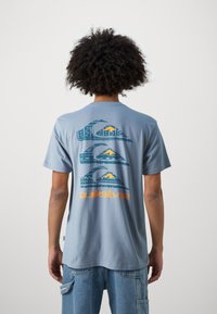Lichtblauw katoenen T-shirt met op de achterkant graphics van bergen en golven in donkergroen en oranje. Eenvoudig crewneck ontwerp en korte mouwen.