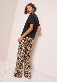 Fekete, rövid ujjú póló, bézs leopárdmintás, bővülő szárú nadrággal párosítva, amely puha anyagot és kontrasztos mintákat mutat be.