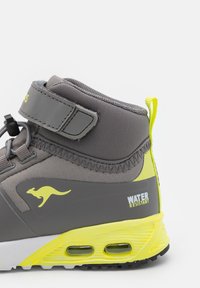 High-top gray sneaker with water-resistant material, yellow accents, padded collar, adjustable strap, and air cushioning in the sole.