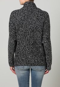 Pull en maille mouchetée noir et blanc avec un col montant, des manches longues et une coupe décontractée. Motif texturé avec finition côtelée au niveau du col.