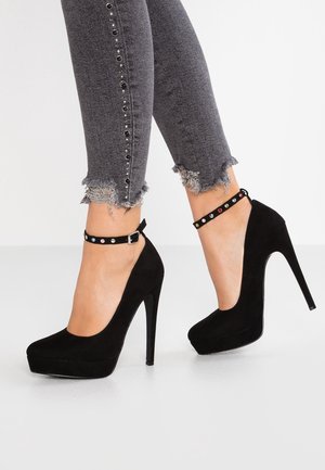 Czarne zamszowe szpilki na platformie z wąskim obcasem. Wyposażone w pasek wokół kostki ozdobiony kolorowymi zdobieniami.