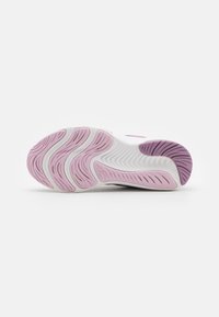 Semelle d'une basket blanche avec des motifs en caoutchouc rose et violet, présentant des rainures courbées pour la traction et la flexibilité.