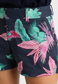Shorts navy avec un motif floral tropical et des feuilles roses et vertes. Matière légère, avec des poches latérales et une coupe droite.