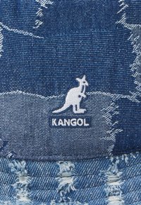 Cappello a secchiello in denim con una tonalità di blu sbiadita, texture strappata e un logo Kangol bianco con un design di canguro.