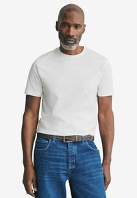 Weißes Baumwoll-T-Shirt mit rundem Ausschnitt, getragen mit blauen Jeans und einem braunen geflochtenen Gürtel, mit klassischer Passform und kurzen Ärmeln.