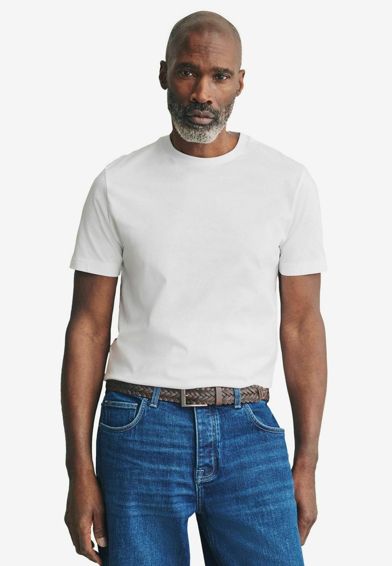Weißes Baumwoll-T-Shirt mit rundem Ausschnitt, getragen mit blauen Jeans und einem braunen geflochtenen Gürtel, mit klassischer Passform und kurzen Ärmeln.