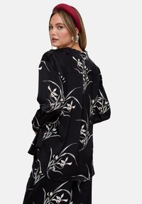 Black shirt with white floral pattern, long sleeves, and loose fit. Contains a back yoke detail and soft, smooth texture.