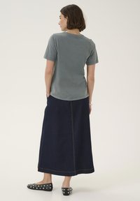 Graues Baumwoll-T-Shirt mit kurzen Ärmeln, kombiniert mit einem langen, dunklen Denimrock. Der Rock zeichnet sich durch sichtbare Nähte und eine gerade Silhouette aus.