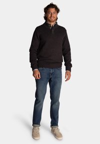 Donkergrijs gebreid sweater met een hoge kraag, blauw geruit overhemd eronder, gecombineerd met blauwe jeans en beige sneakers. Casual pasvorm.