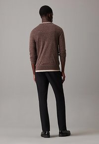 Maglione marrone con texture, maniche lunghe, collo a giro e un accento bianco a contrasto all'orlo, abbinato a pantaloni neri e scarpe.