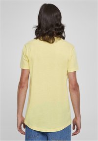 Gul kortærmet T-shirt med rund kant og en afslappet pasform. Blød tekstur med minimal syning, båret med blå denimshorts.
