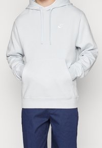 Ljusblå huvtröja med framficka, ribbade muddärmar och en vit Nike-logotyp på bröstet. Mjukt, strukturerat tyg.