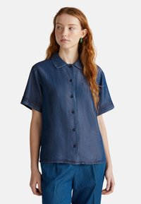 Camisa de mezclilla de manga corta en azul oscuro, con cierre de botones en la parte delantera, cuello y puños doblados. Textura suave con un detalle de costura mínimo.
