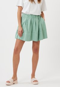 Mintgrön kjol med veck och resår i midjan, tillverkad av mjukt tyg. Matchas med ljusrosa slidesandaler.