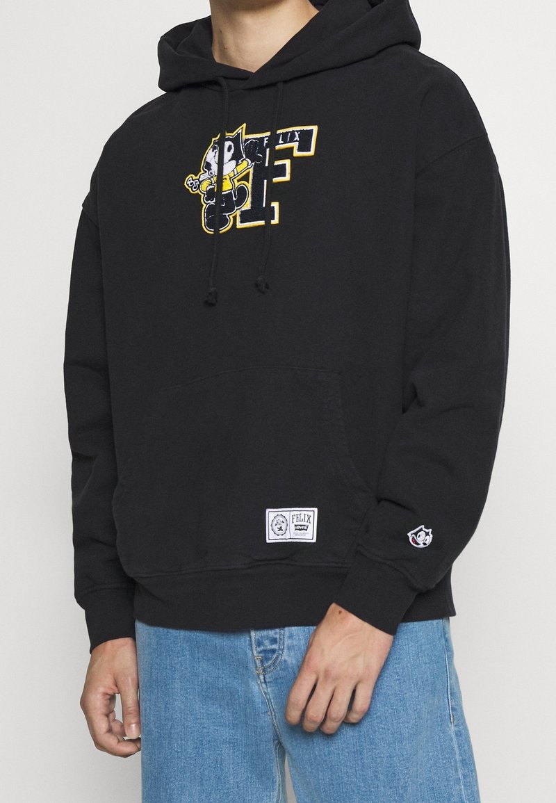 Černá mikina s kapucí s grafikou Felixe Kočky, obsahuje kapuci se stahovací šňůrkou, přední kapsu a logo nášivku na lemu. Volný střih.