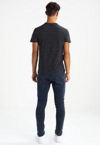 Pánské tričko s krátkým rukávem z tmavě šedé látky, spárované se slim-fit modrými džíny a bílými botami. Jednoduchý design s kulatým výstřihem.